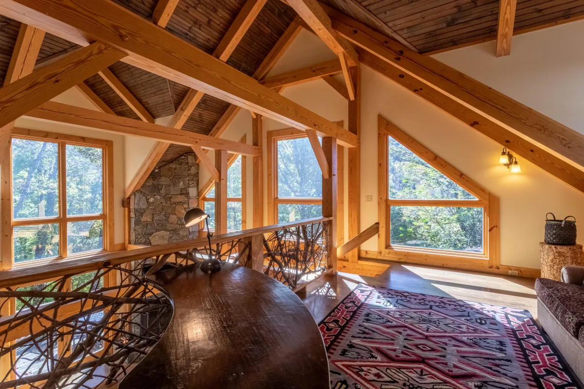 A bright living area highlighted by large windows with sweeping views, wooden beams, a stone accent wall, and a decorative rug. The space feels inviting and directly connects guests to the natural surroundings.