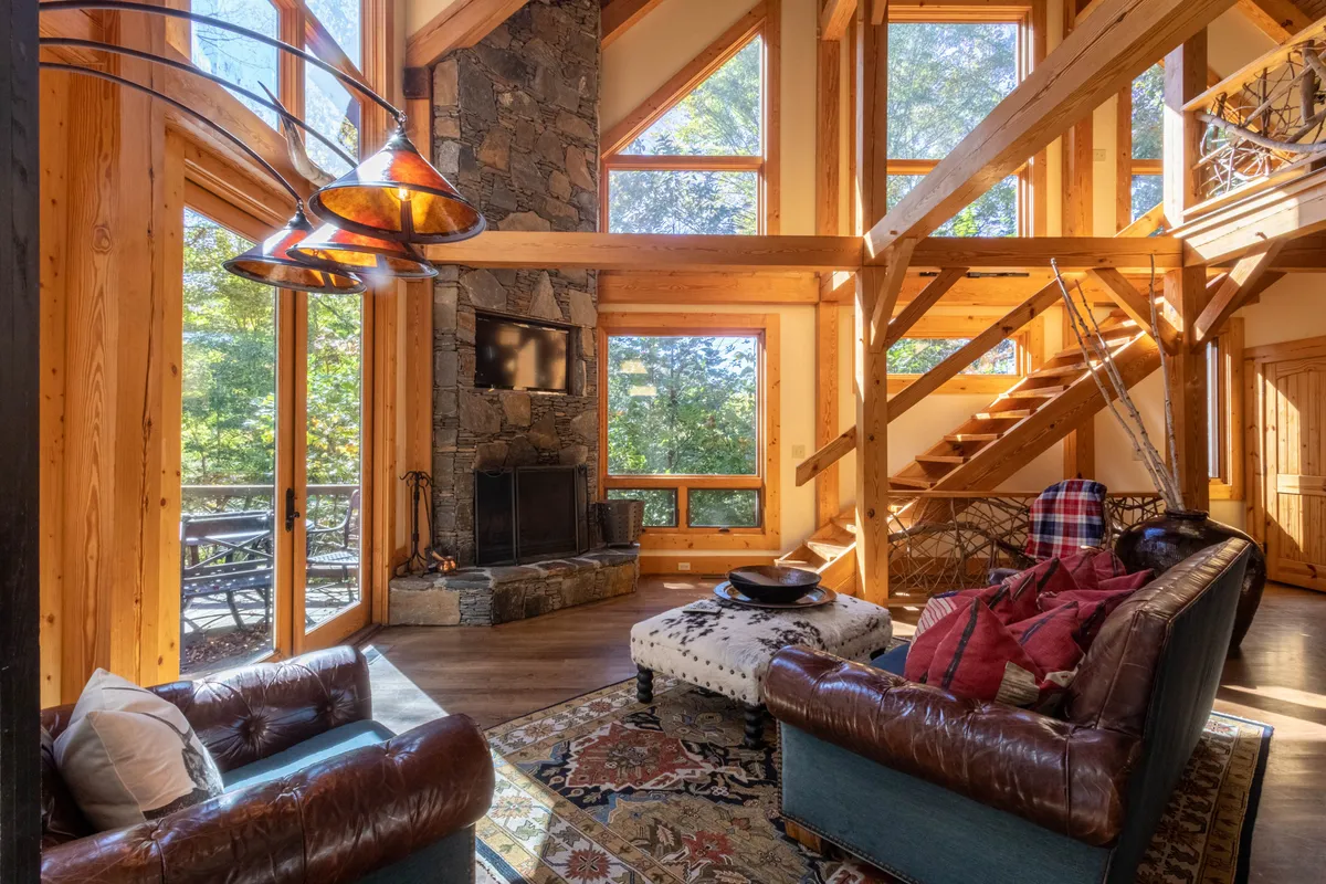 A cozy interior with a large stone fireplace, expansive windows revealing mountain scenery, and a comfortable seating area. The warmth of the room is complemented by wooden beams and a casual, homey atmosphere, ideal for families and groups.
