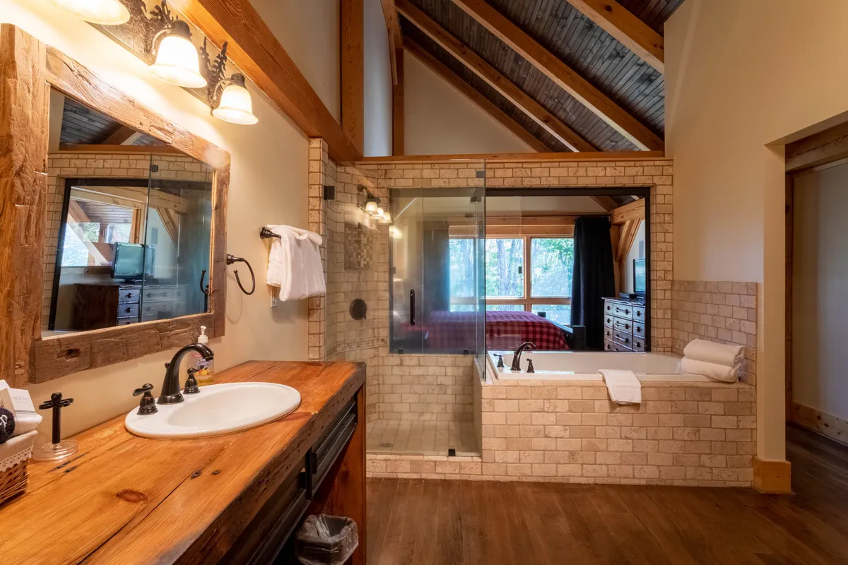 A serene bathroom featuring a freestanding bathtub next to a large window with views of nature, a glass shower enclosure, and a wooden vanity. Natural light pours in, emphasizing the spa-inspired atmosphere.