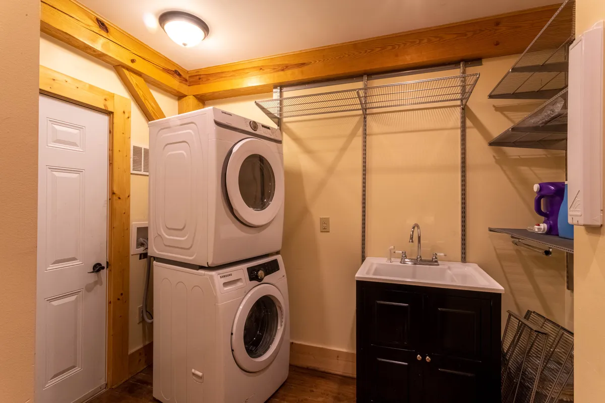A functional laundry area featuring a washer and dryer, utility sink, and shelving for organizing cleaning supplies. The space is well lit and designed for practical use after outdoor activities.