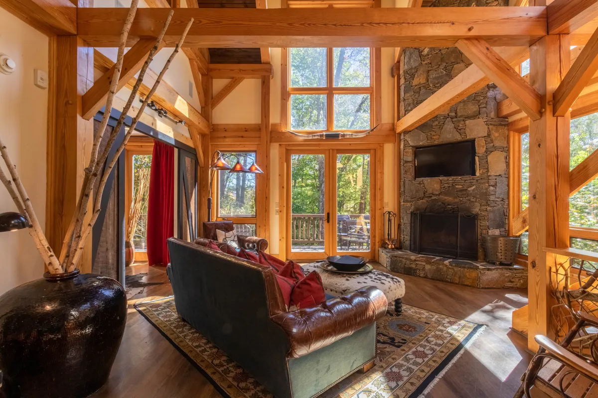 A welcoming Great Room featuring a large stone fireplace framed by expansive windows. The comfortable seating area is arranged to foster conversation and relaxation, while a decorative lamp adds a cozy touch. Natural light streams in, providing views of the outdoors and enhancing the room's warm, inviting atmosphere.