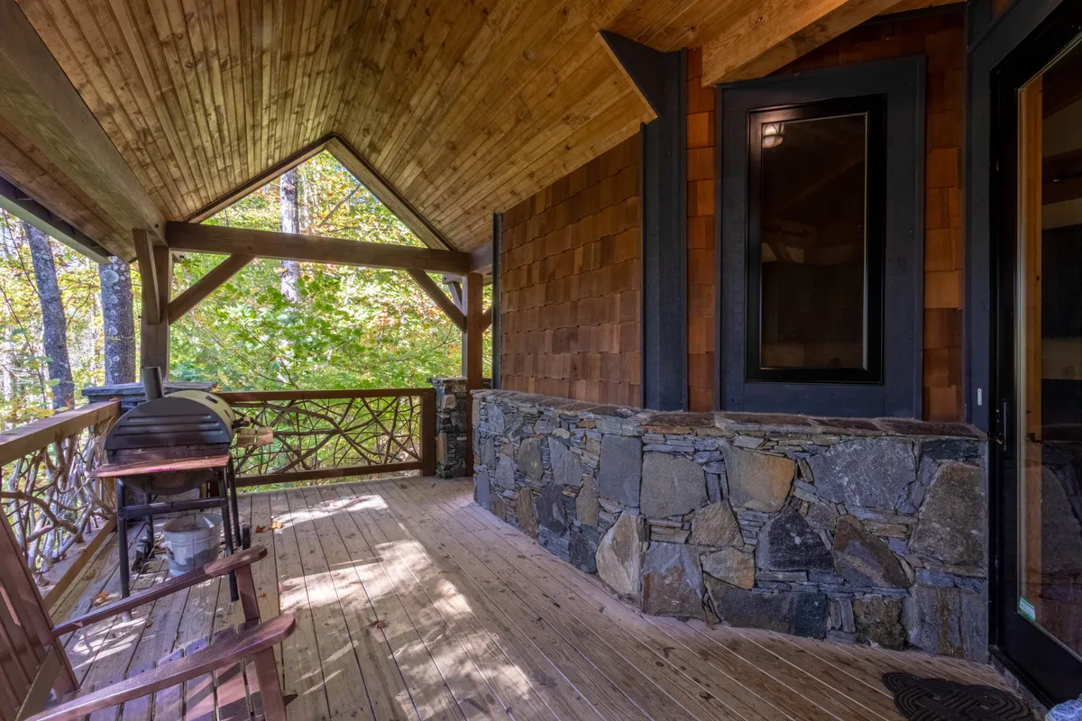 This image presents another inviting outdoor space— a wooden deck with a stone wall, grill, and wooden chairs—all surrounded by tranquil mountain scenery. It's ideal for sunset dinners, morning coffee, or stargazing—activities that reflect both relaxation and elevated living.