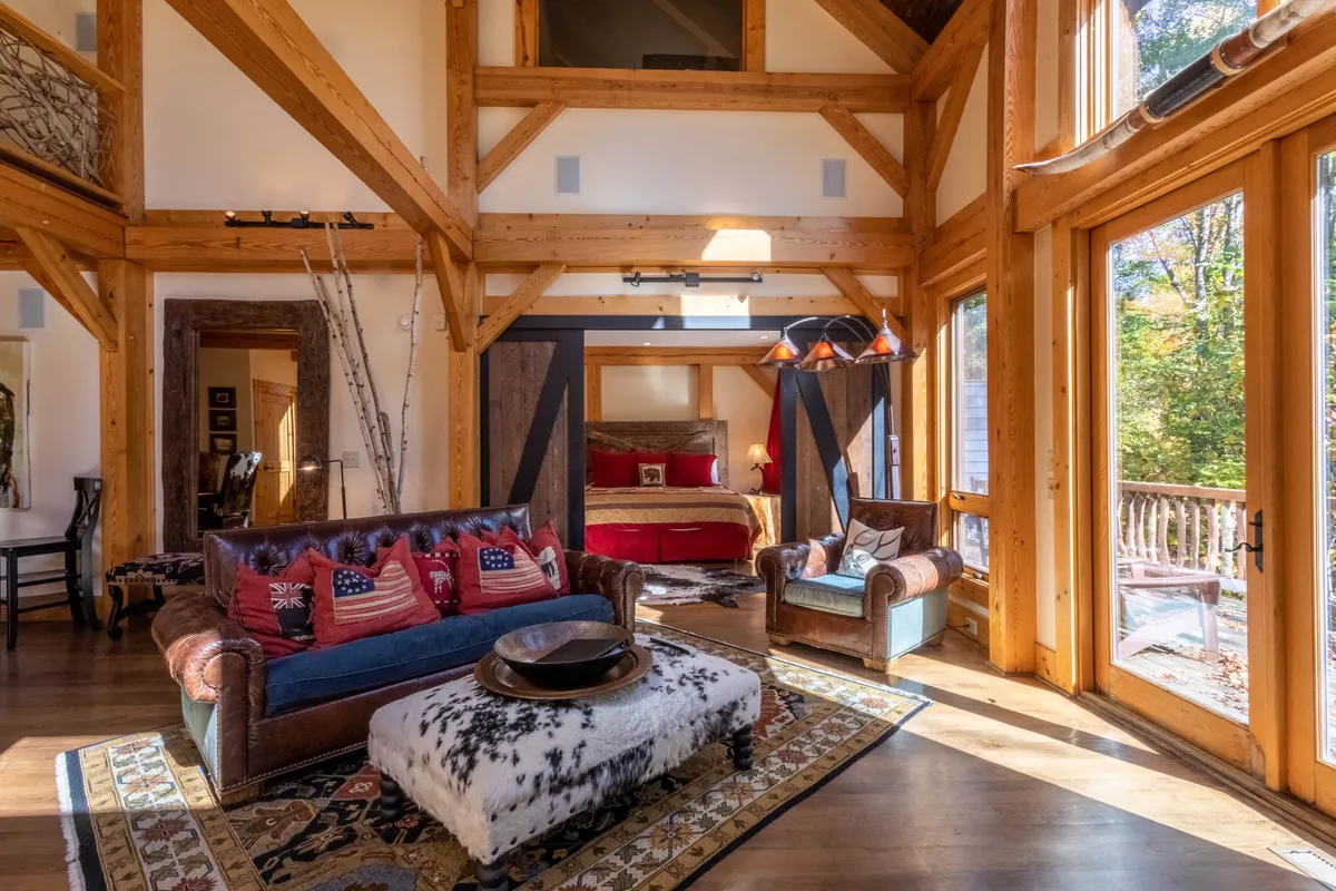 A spacious living area featuring a large leather sofa, rustic wooden beams, and bright windows that invite in natural light. The setting supports cozy afternoons, reading, and group gatherings, with the fire as a focal point.