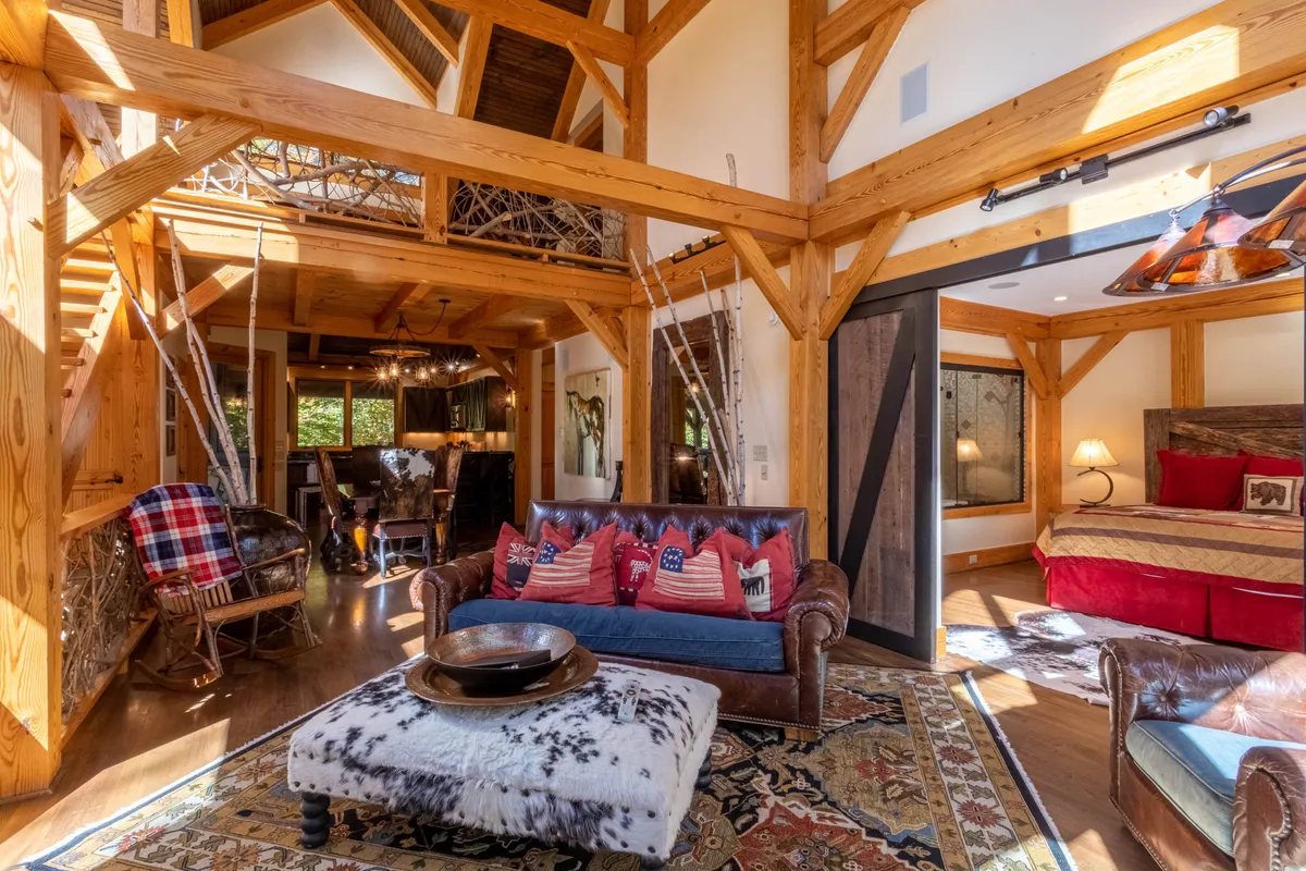 A warmly lit living room with rustic wooden beams, a plush leather sofa, a decorative rug, and festive touches. The scene is inviting and hints at lively gatherings, relaxing moments by the fireplace, and seasonal celebrations.