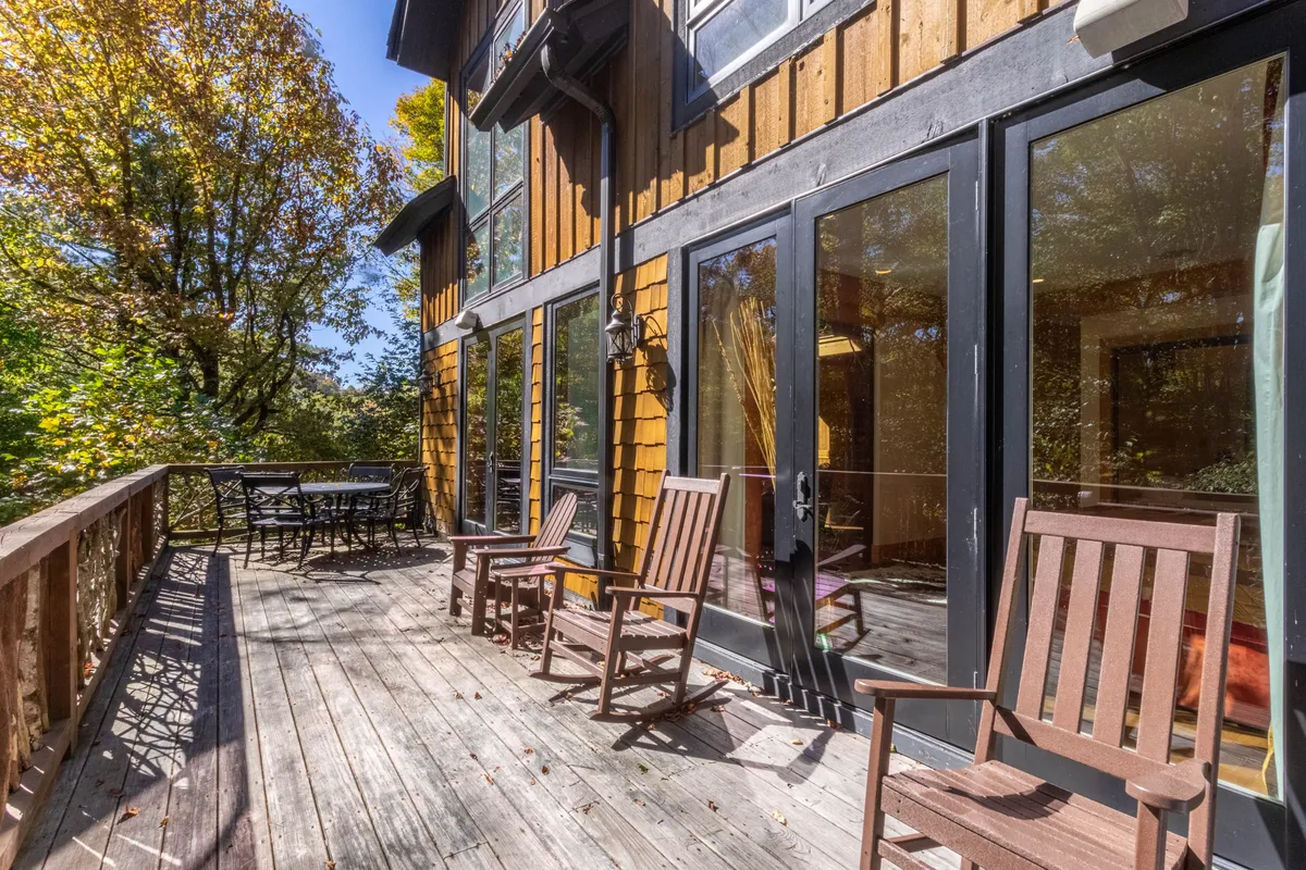 A tranquil wooden deck bordered by trees, with comfortable outdoor seating and large glass doors connecting inside and out. The deck offers a peaceful spot for relaxing after a day of adventure, and hints at the community spaces where families and groups gather.