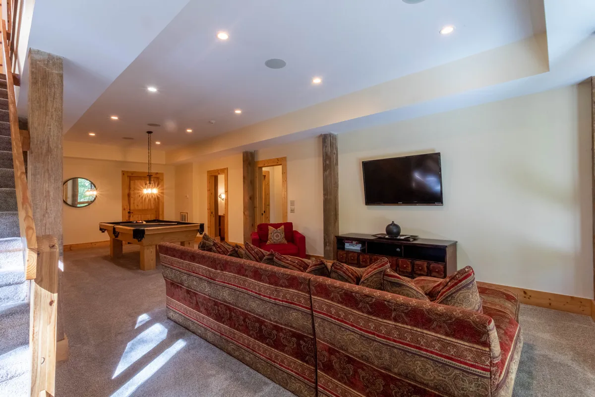 This image features a spacious den with a large patterned sofa, pool table, and entertainment center. The setting is casual and inviting, ideal for both lively games of billiards and cozy movie nights. The decor balances rustic charm with comfort, and the layout encourages group activities and relaxation.